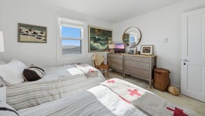 A bedroom with two beds, a dresser, a mirror, and artwork on the walls.