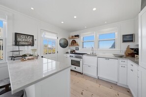 Une cuisine moderne avec des meubles blancs, un îlot central, une cuisinière et un évier.