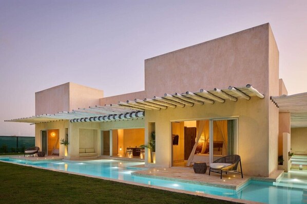 Une maison moderne dotée d’une piscine, d’un espace salon extérieur et d’un patio couvert.