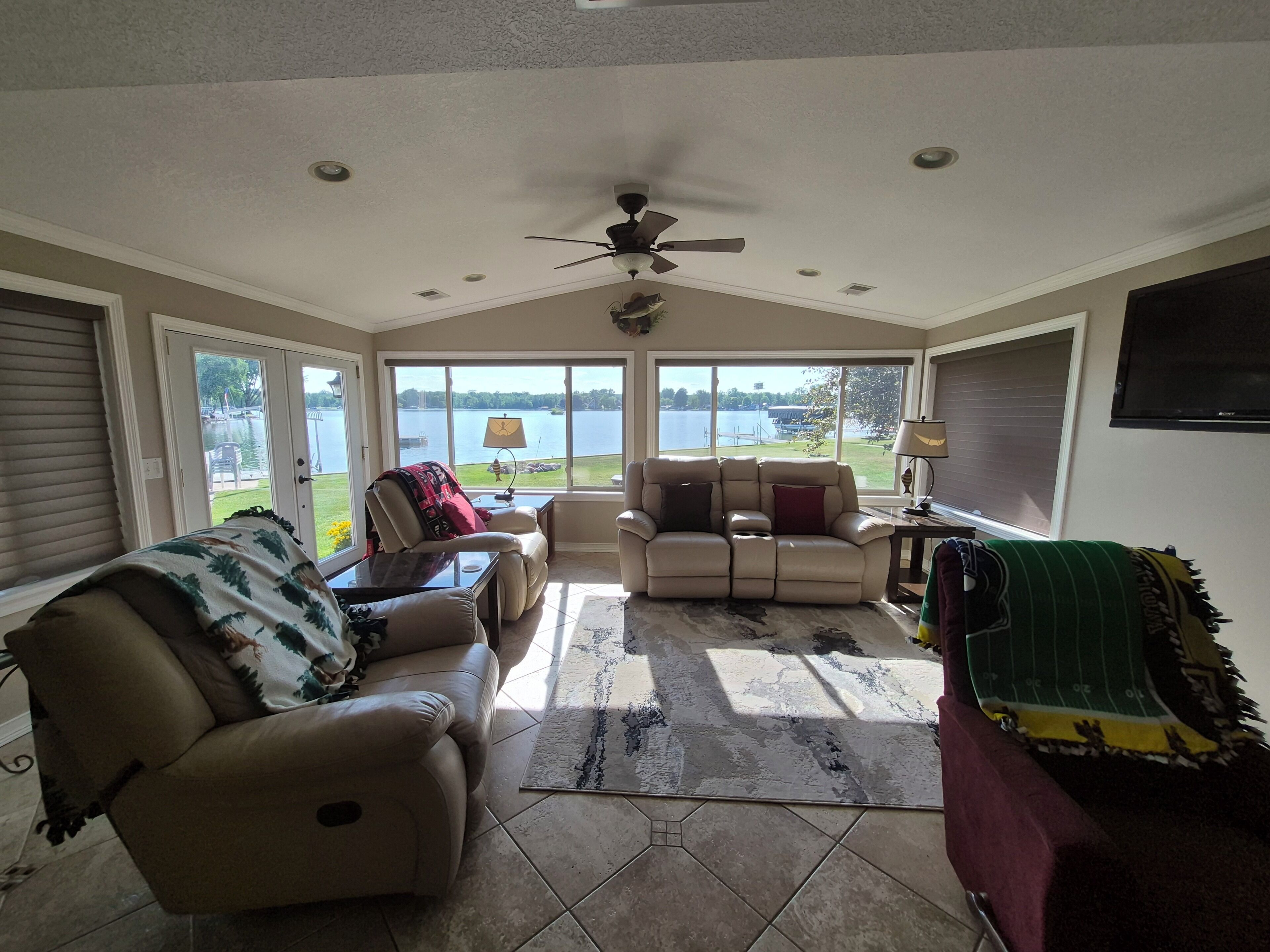 A sunroom with a ceiling fan, large windows, a leather sofa, a recliner, and a view of a lake.