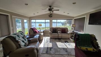 A sunroom with a ceiling fan, large windows, a leather sofa, a recliner, and a view of a lake.