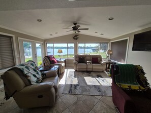 A sunroom with a ceiling fan, large windows, a leather sofa, a recliner, and a view of a lake.