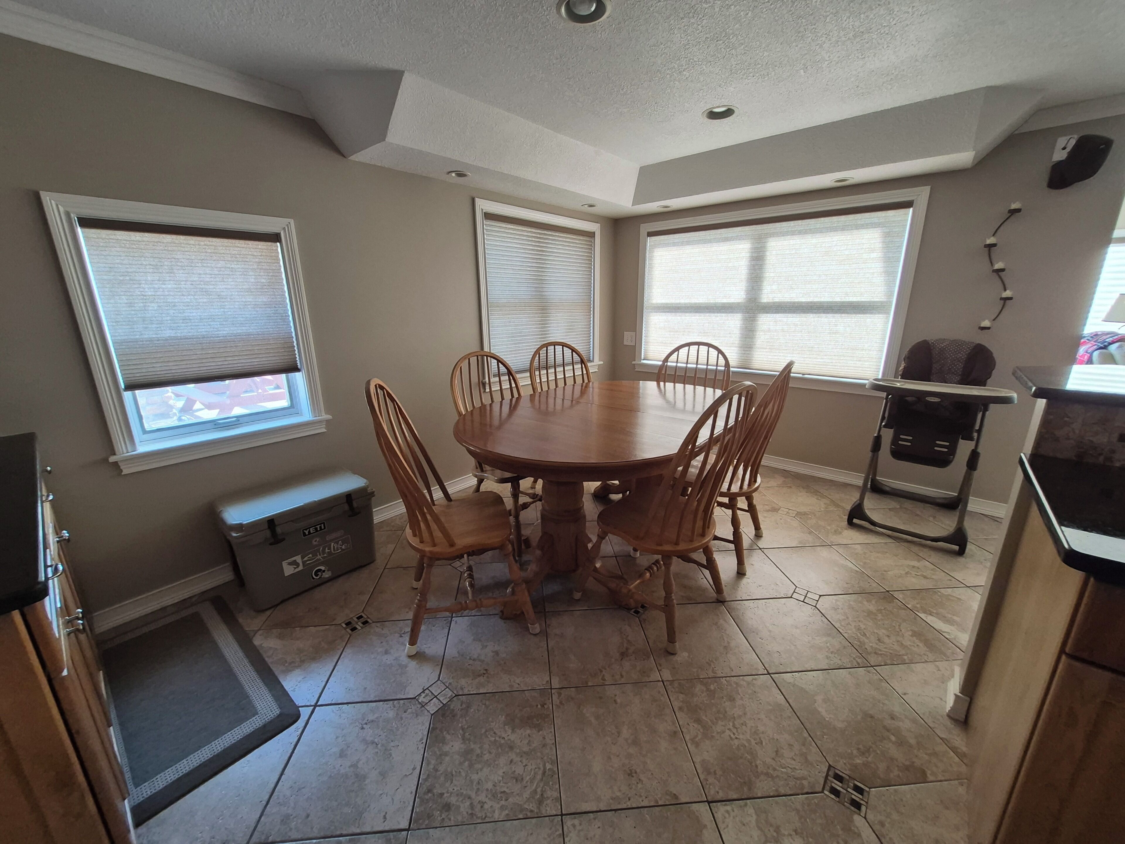 A dining area with a round table and six chairs, a baby high chair, and a storage unit.