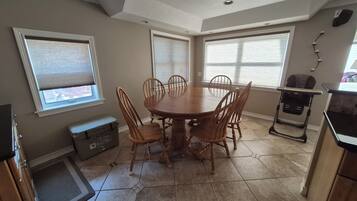A dining area with a round table and six chairs, a baby high chair, and a storage unit.