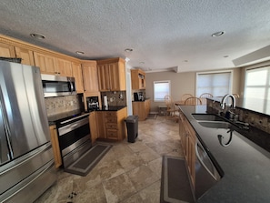 A modern kitchen with wooden cabinets, stainless steel appliances, and a dining area with a window. - Stunning Lakefront house + guest house on beautiful Littlefield Lake (Lake)