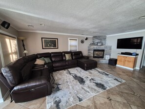 A living room with a sectional sofa, a fireplace, a flat-screen TV, and a stone fireplace surround. - Stunning Lakefront house + guest house on beautiful Littlefield Lake (Lake)