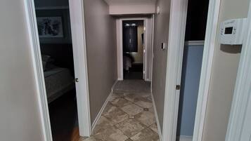 A hallway with a tiled floor, a door on the left, and a wall-mounted thermostat on the right.