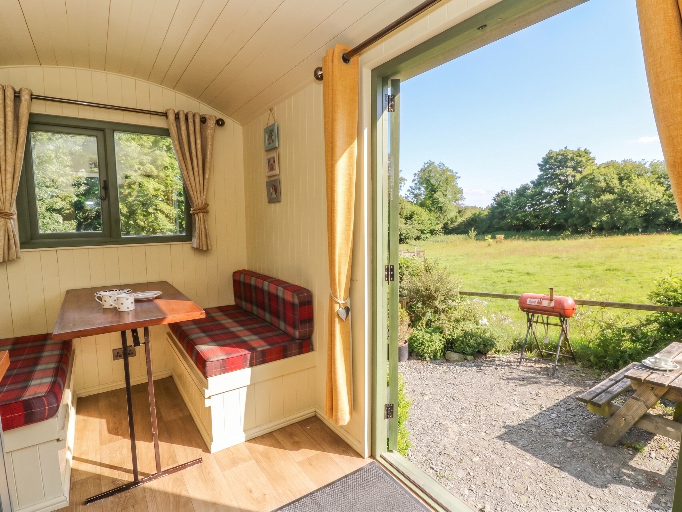 Quarto aconchegante com um banco, uma mesa e vista para um campo gramado.