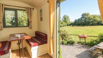 Quarto aconchegante com um banco, uma mesa e vista para um campo gramado.