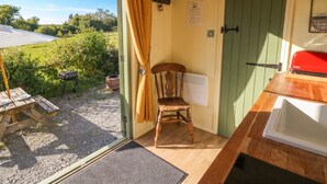 Una habitación con una silla de madera, una mesa, una puerta verde y vistas al exterior.