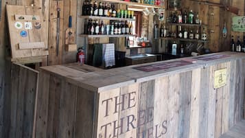 A rustic bar with wooden shelves stocked with various bottles and a sign reading 'THE THIRD SPANELS'.