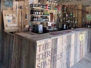 Un bar rústico con estantes de madera llenos de diferentes botellas y un letrero que dice 'THE THIRD SPANELS'.
