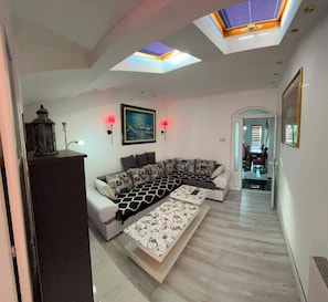 Un salon moderne avec un canapé d’angle, une table basse, un tableau et une lucarne.