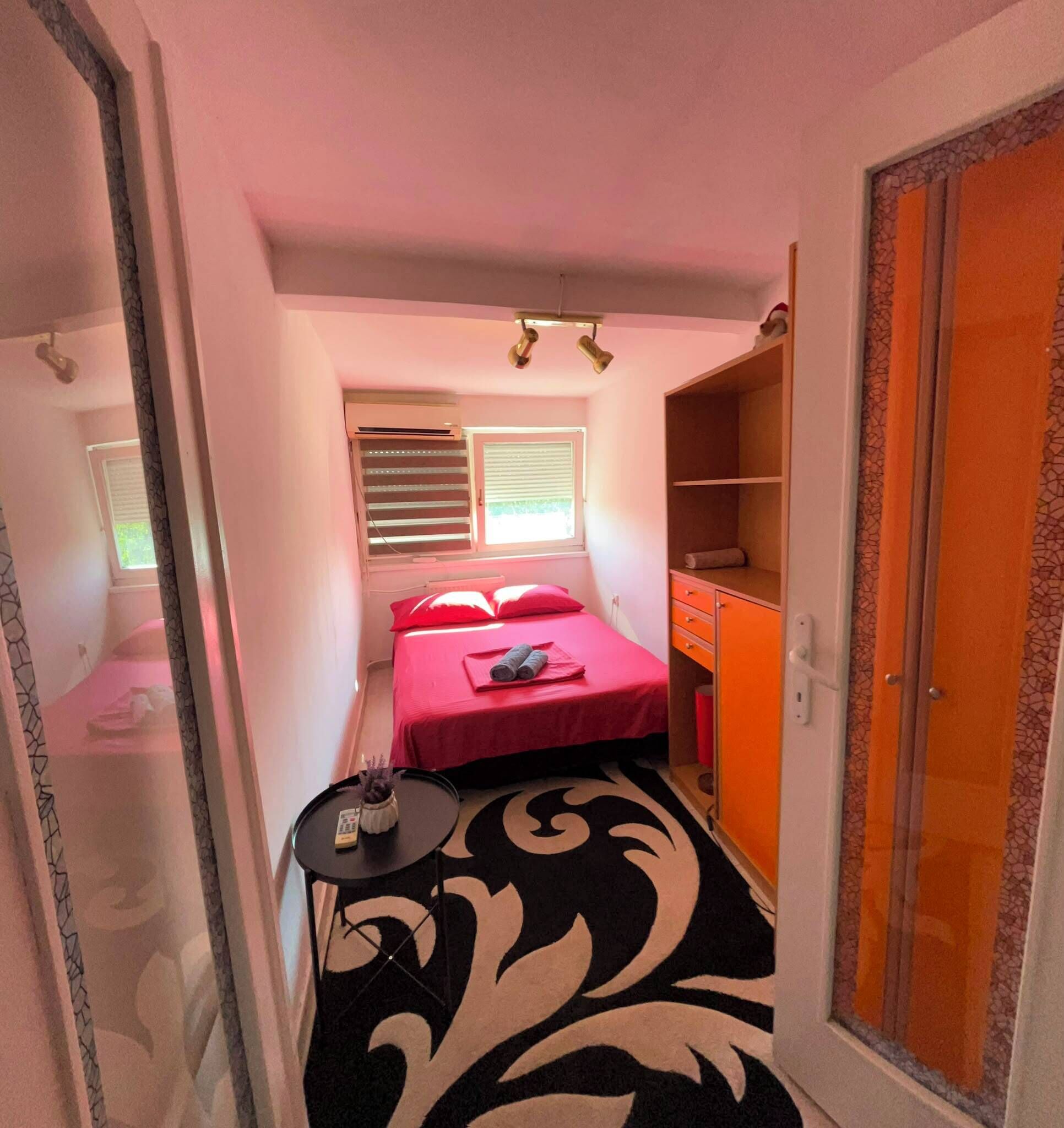 Habitación compacta con cama, una pequeña mesa con un florero, un armario y una ventana con persianas.