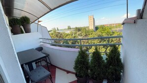 A balcony with a table and chairs, potted plants, and a view of buildings and trees. - Cozy 2-bedroom apartment in adorable Pančevo with AC (Pančevo)