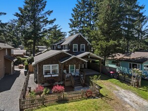 A two-story house with a covered porch, a fenced yard, and a driveway. - Coastal cottage with hot tub, close walk to beach (Cannon Beach)
