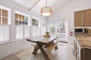 A kitchen with a wooden table, white cabinetry, and a hanging light fixture. - Coastal cottage with hot tub, close walk to beach (Cannon Beach)