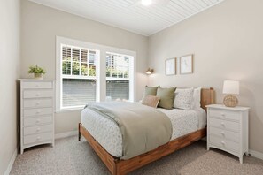 A bedroom with a bed, a nightstand, a dresser, and a window with blinds. - Coastal cottage with hot tub, close walk to beach (Cannon Beach)