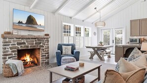 Una sala de estar acogedora con chimenea de piedra, un sillón cómodo, una mesa de centro y vista a la playa a través de un amplio ventanal.