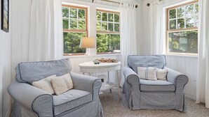 Una habitación con dos sillones a rayas, una mesita redonda y amplias ventanas con cortinas blancas.