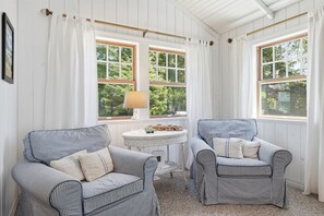 A room with two striped armchairs, a small round table, and large windows with white curtains. - Coastal cottage with hot tub, close walk to beach (Cannon Beach)
