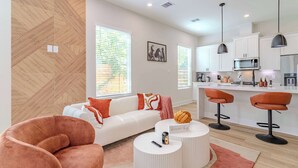 Een moderne woonkamer met een bank, twee ronde salontafels en een keukenhoek met barstoelen.