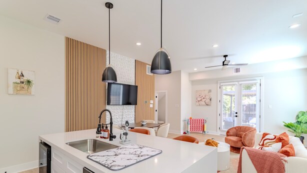 Een moderne keuken met een centraal eiland, een eethoek met oranje stoelen, en een woonkamer met een bank en een groot raam.