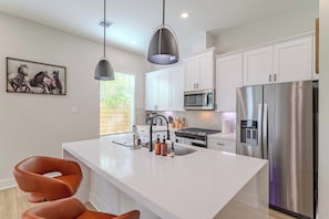 A modern kitchen with white cabinets, stainless steel appliances, a central island with seating, pendant lighting, and a window with blinds. - Spring Branch 3BR - Mins to CityCentre (Houston)