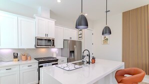 Een moderne keuken met witte kasten, een centraal eiland, roestvrijstalen apparatuur en hanglampen.