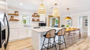 Une cuisine moderne avec des meubles blancs, un îlot central, des tabourets de bar et des luminaires suspendus.