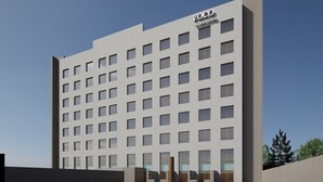 En moderne hotelbygning med en flad facade, mange vinduer og et poolområde i forgrunden.