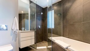 Un bagno moderno con doccia vetrata, una vasca da bagno bianca e un lavandino bianco.