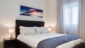 Un letto rifatto con cura, una testiera scura, due lampade ai lati e un quadro con una vista sulla città.