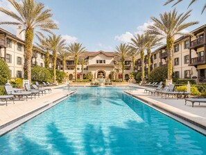 Ein Pool mit Liegestühlen und Palmen, umgeben von mehrstöckigen Gebäuden mit Balkonen.