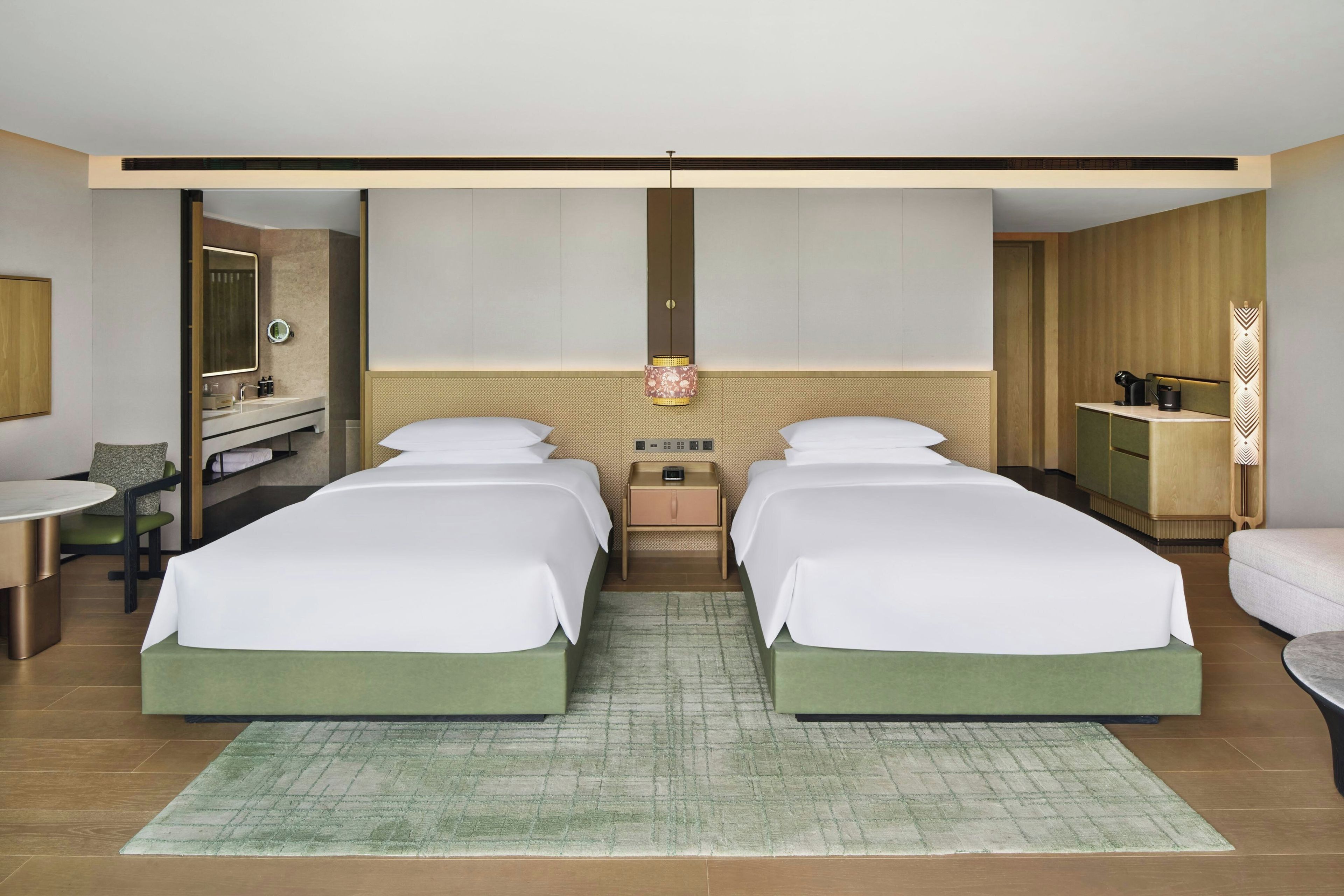 Habitación de hotel con dos camas, una sala de estar con mesa y sillas, un baño con espejo y un escritorio con lámpara.