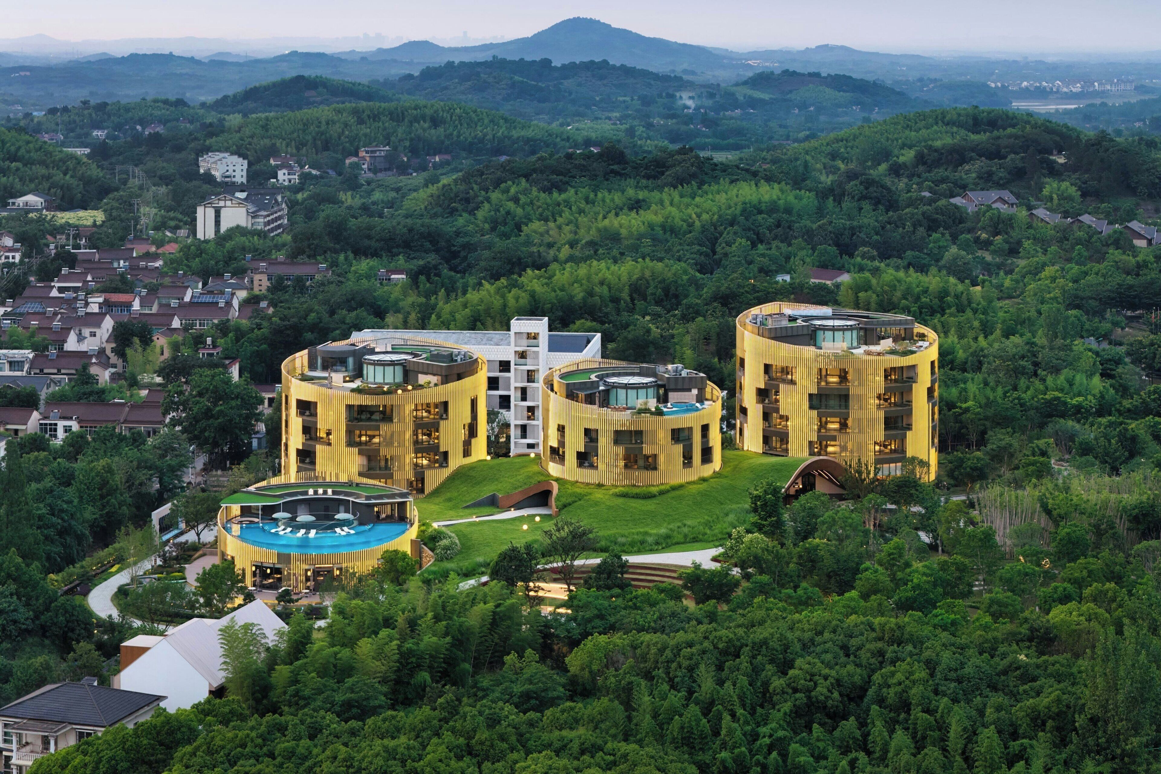 Un hôtel moderne à l’architecture circulaire, entouré d’une végétation luxuriante et situé dans un paysage vallonné.