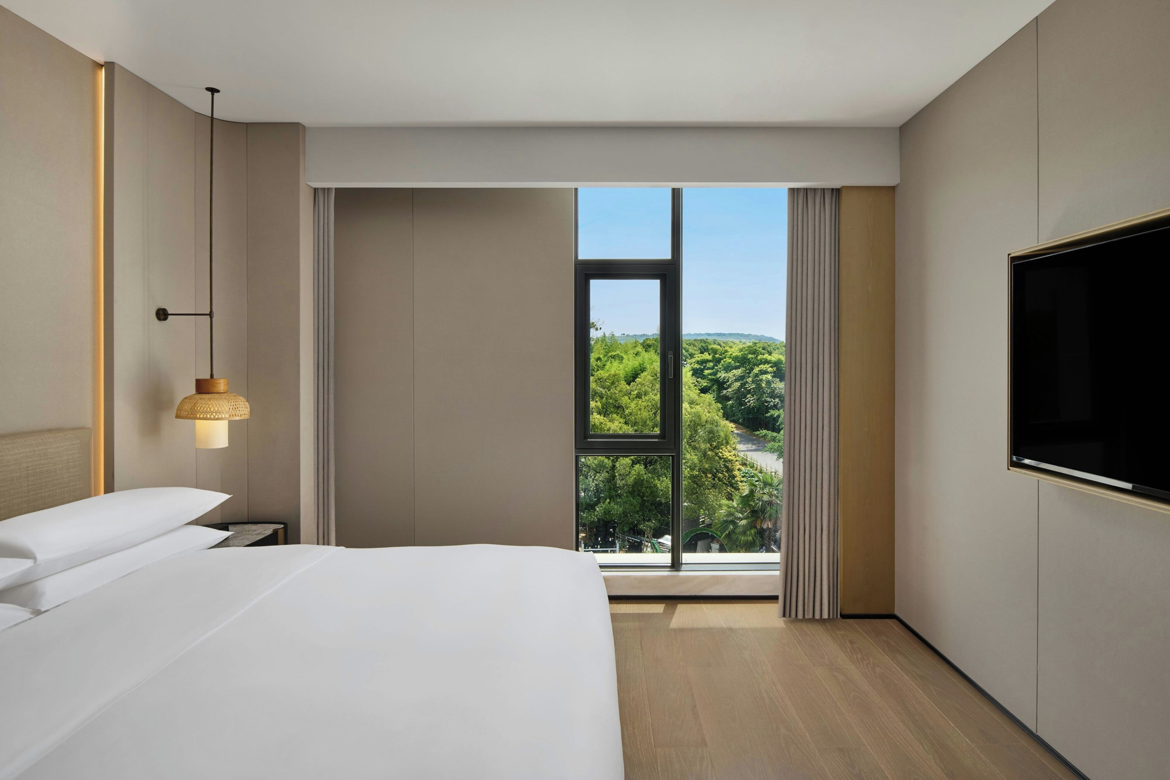Una habitación de hotel moderna con una cama grande, televisión y ventana con vista a la ciudad.
