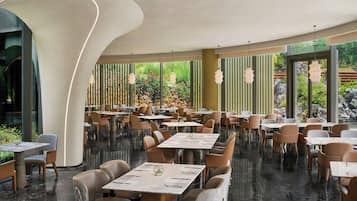 A modern restaurant interior with round tables, cushioned chairs, and pendant lighting.