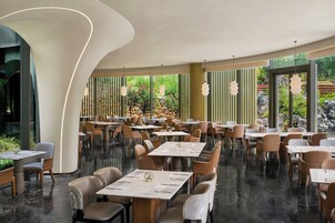 A modern restaurant interior with round tables, cushioned chairs, and pendant lighting.