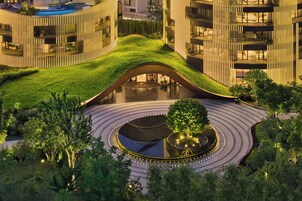 Un edificio moderno con un diseño de techo curvo único, un patio central con una fuente circular y follaje circundante.