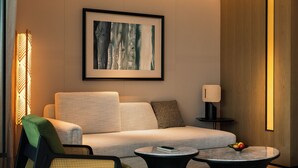 Un hotel moderno con sofá, dos mesitas auxiliares, una silla, una lámpara y una obra de arte enmarcada en la pared.