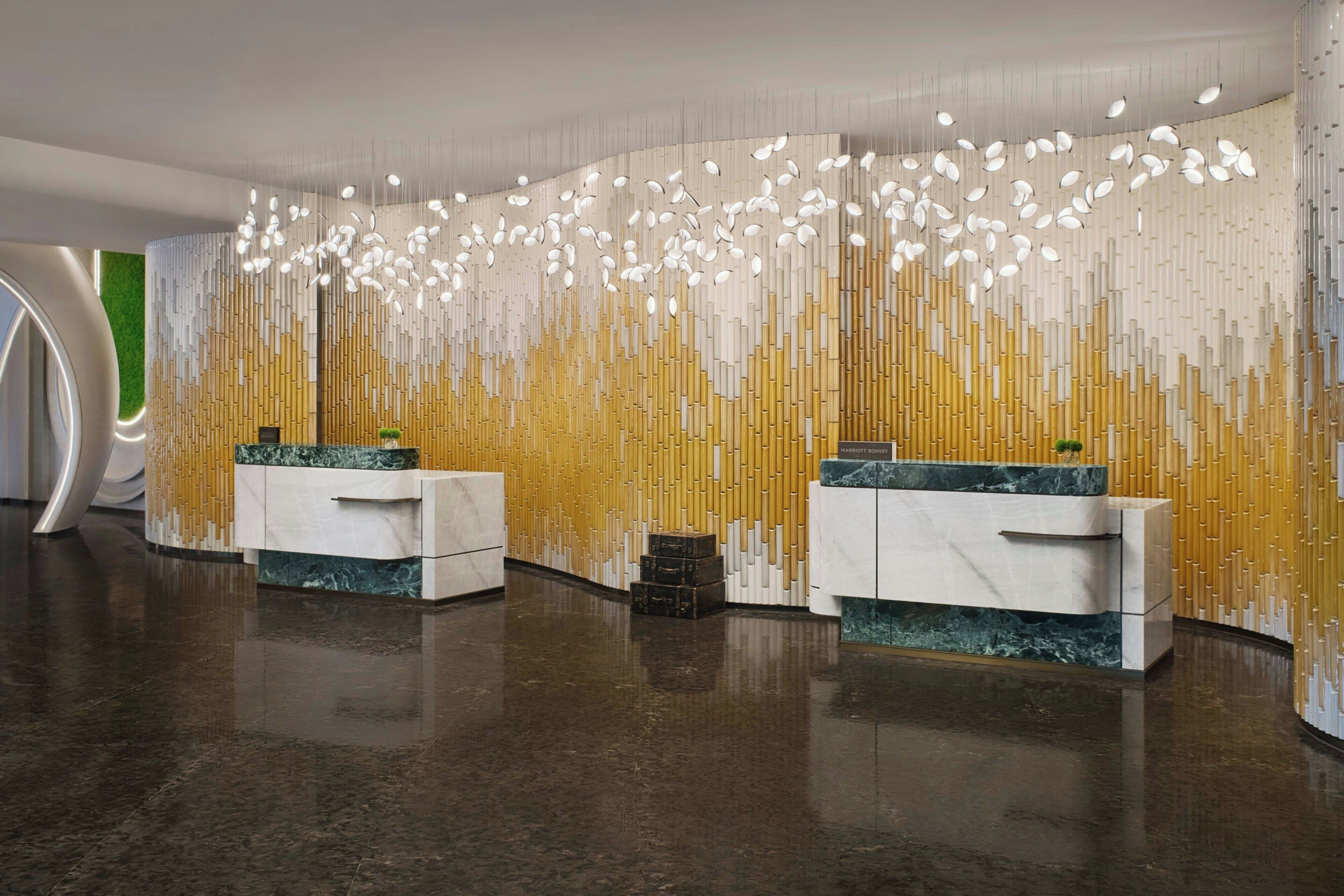 A modern reception area with marble counters, a vertical bamboo wall, and a ceiling with hanging light fixtures.