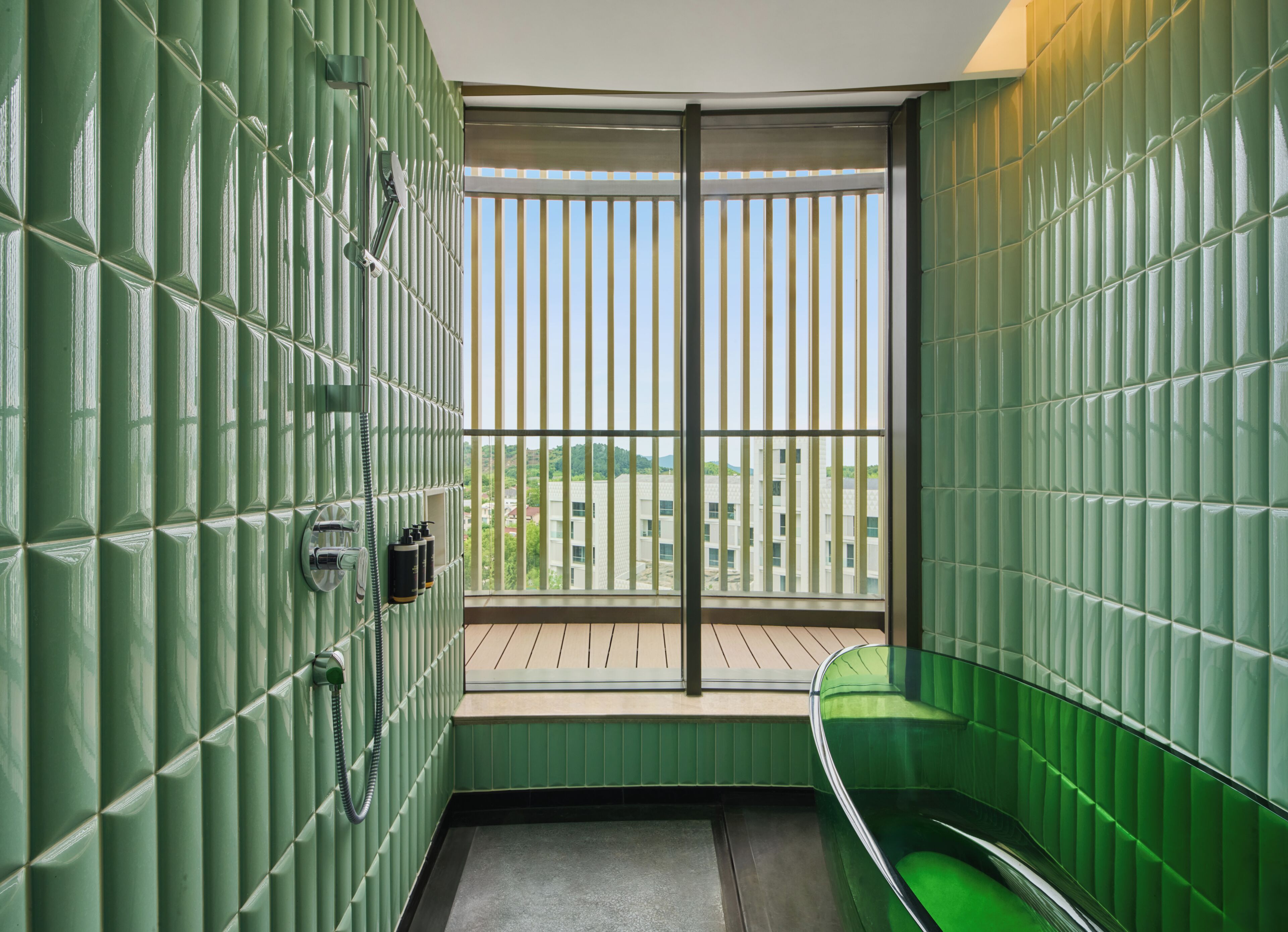 A bathroom with green tiled walls, a wooden floor, and a window with vertical blinds.