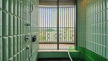A bathroom with green tiled walls, a wooden floor, and a window with vertical blinds.