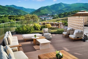 Una terraza con mobiliario exterior, vista a un pueblo y montañas al fondo.