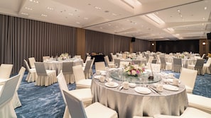 Un salón de banquetes con mesas redondas, sillas blancas y una alfombra azul.