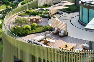 Un patio moderno al aire libre con una terraza de madera curva, espacios de descanso y una piscina.