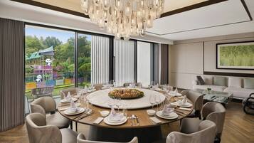 Comedor con una mesa redonda dispuesta para seis personas, sillas alrededor, una gran lámpara de araña y vistas a un jardín con zona de juegos.