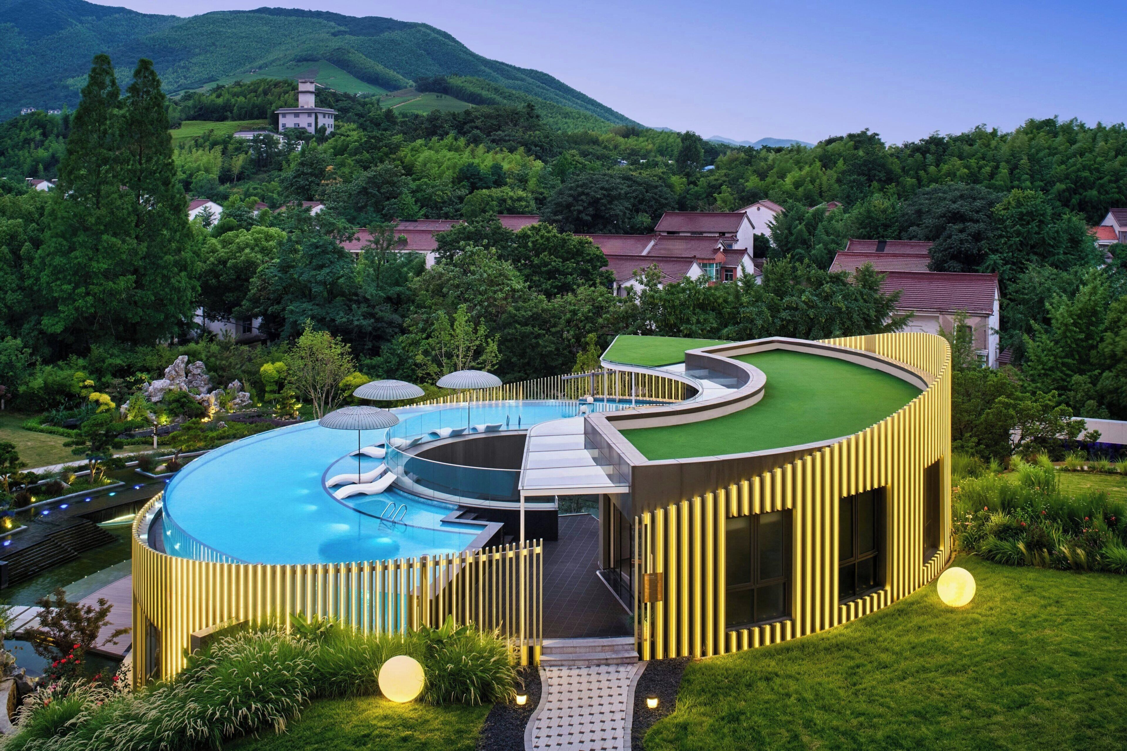 Un hotel moderno con piscina circular, rodeado de exuberante vegetación y un telón de fondo montañoso.