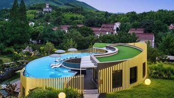 Un hotel moderno con piscina circular, rodeado de exuberante vegetación y un telón de fondo montañoso.